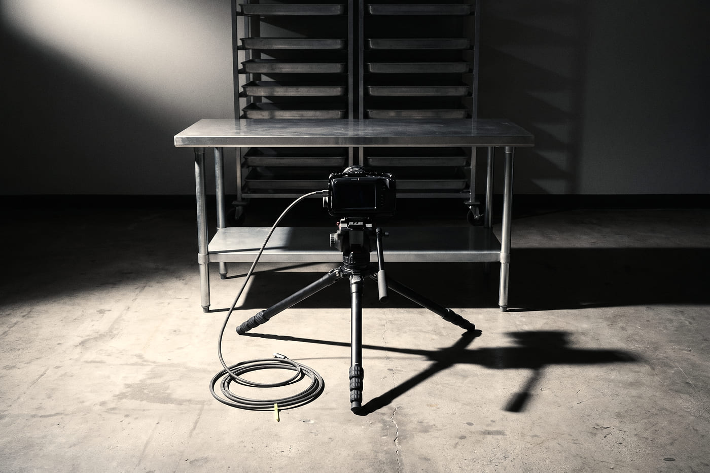 A camera locked to a tripod on a factory floor, aimed at an empty steel workbench